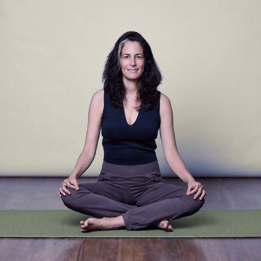 אבישג אורן יושבת בישיבה מזרחית על מזרן יוגה